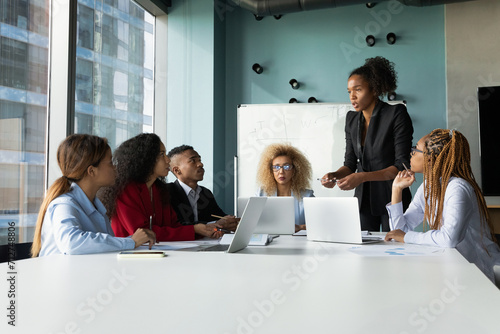 Young diverse multiethnic business team gather on briefing in modern office under lead of afro american female boss. Skilled black woman ceo hold meeting at boardroom speak set tasks to staff members