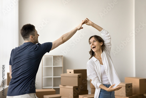 Cheerful young boyfriend and girlfriend beginning living together, having fun at relocation party, dancing to music with paper boxes in background, smiling, laughing