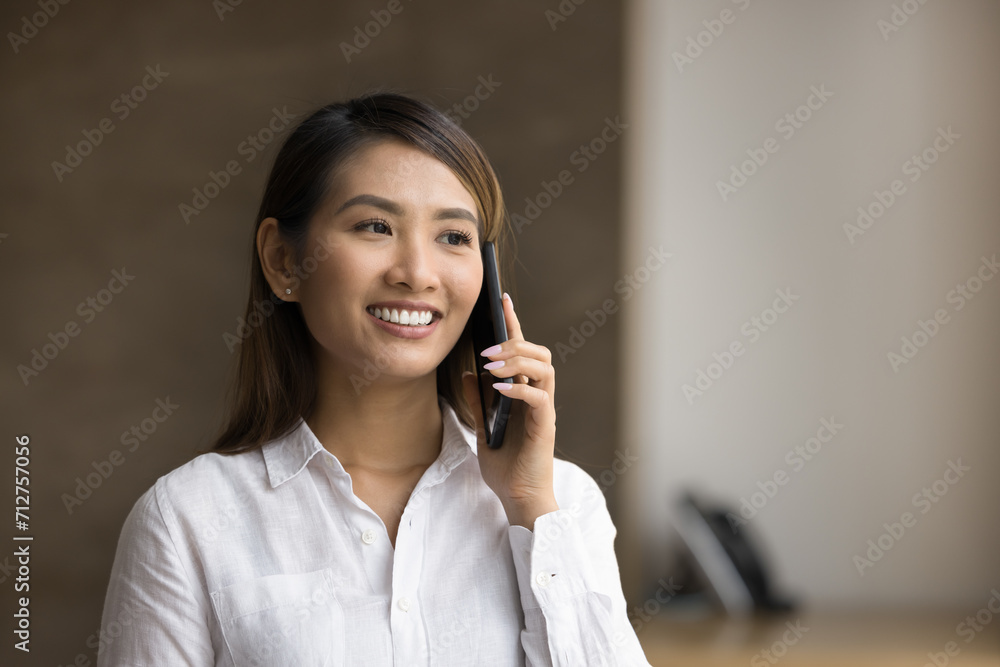 Cheerful young beautiful Asian manager talking to customer on mobile phone, smiling, enjoying connection, conversation, making job call, using wireless technology for work communication Cheerful young beautiful Asian manager talking to customer on mobile phone, smiling, enjoying connection, conversation, making job call, using wireless technology for work communication