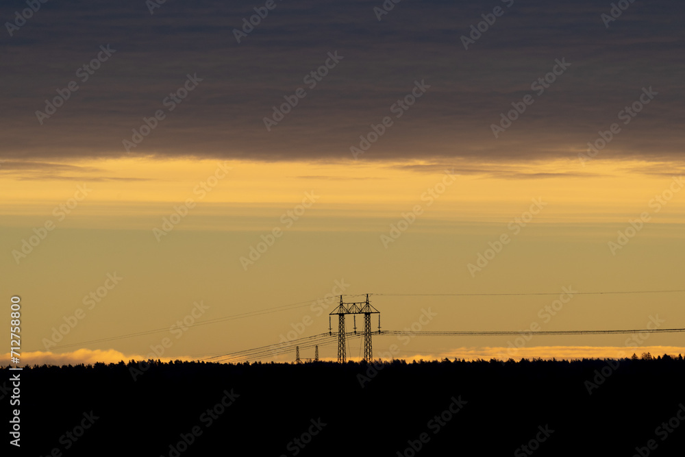 Sunset over tree silhouettes and power line pylon