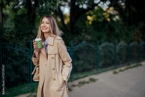 Woman smiling on the street while drinking coffee to go.