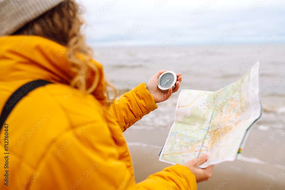 Obraz na płótnie Traveler explorer young woman holding compass and a map in her hands on the beach near the sea. Adventure, vacation concept. Active lifestyle. w salonie