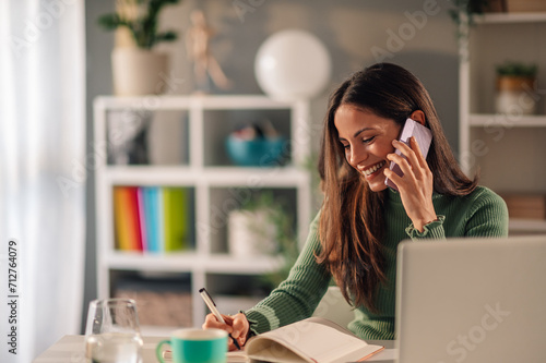 Businesswoman working at home while talking on a phone and taking notes photo