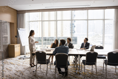 Canvastavla Young Asian business leader woman presenting project to diverse team of managers, telling management strategy to colleagues, talking to workgroup in modern office boardroom interior