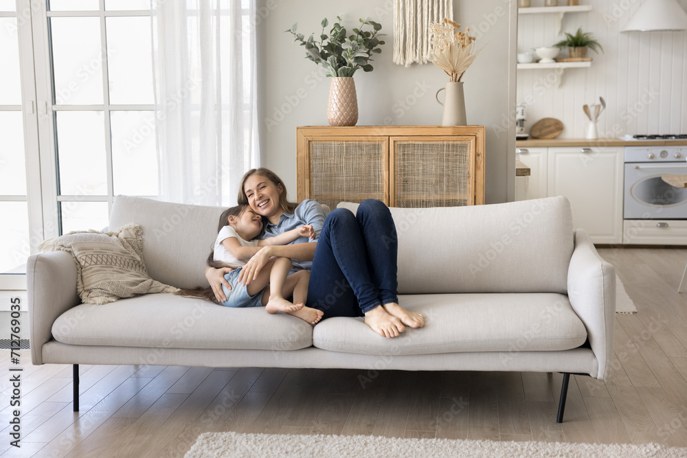 Sweet moments of loving mother and little daughter. Cute preschooler kid girl relaxing on sofa cuddling with loving mom, laughing, play, sit on couch, enjoy carefree rest in cozy living room at home Sweet moments of loving mother and little daughter. Cute preschooler kid girl relaxing on sofa cuddling with loving mom, laughing, play, sit on couch, enjoy carefree rest in cozy living room at home