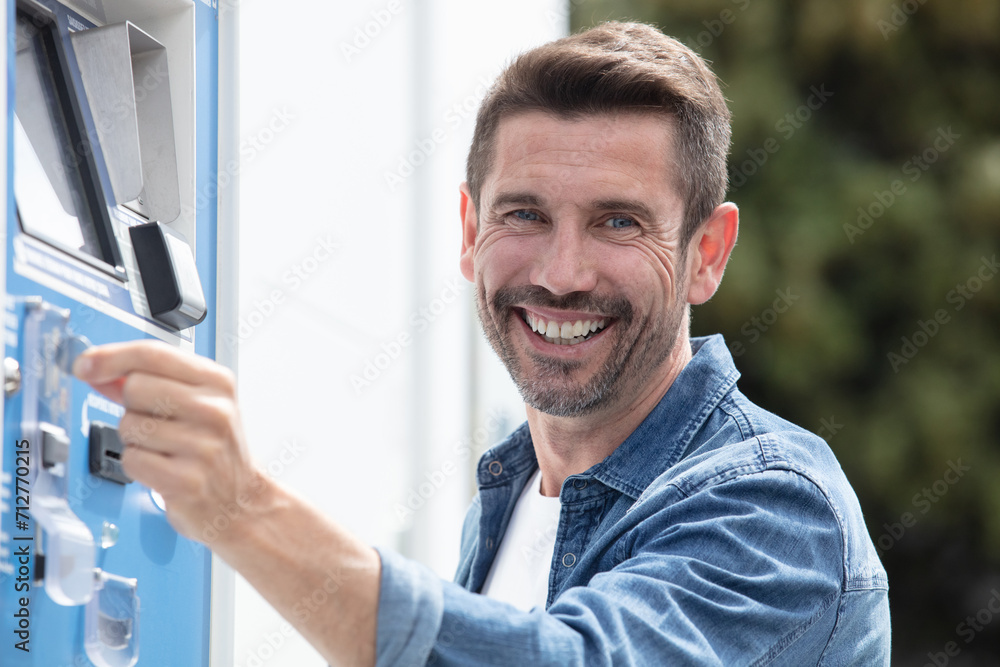 Fototapeta premium adult man putting money in a downtown parking meter