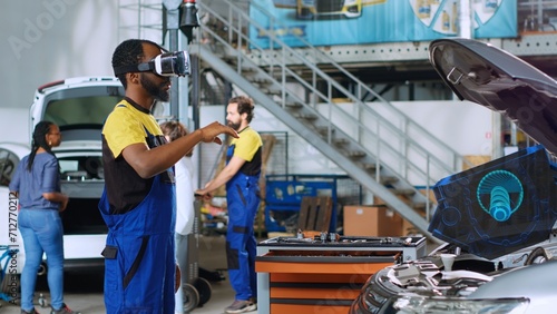 Certified engineer in repair shop using advanced virtual reality technology to visualize car mechanical component in order to fix it. Garage expert wearing vr glasses while mending broken vehicle