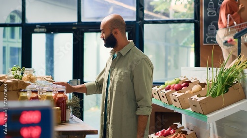 Young man shops at local supermarket, supporting local vendors and choosing eco friendly fruits and veggies from shelves. Middle eastern client smells spices placed in nonpolluting jars. photo