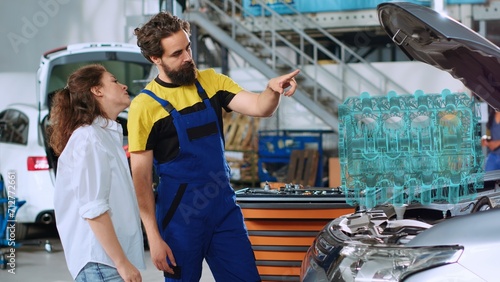 Engineer in auto repair shop using holographic augmented reality to show customer malfunctioning engine inside car. Licensed garage worker using futuristic AR tech to project vehicle parts for client
