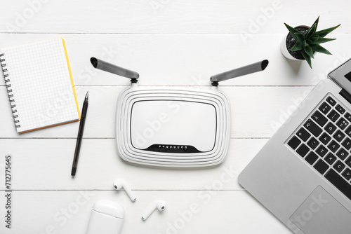 Modern wi-fi router with laptop and earphones on white wooden background