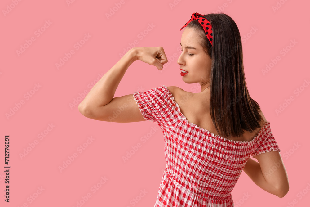 Fototapeta premium Portrait of strong pin-up woman showing muscles on pink background. Women's History Month