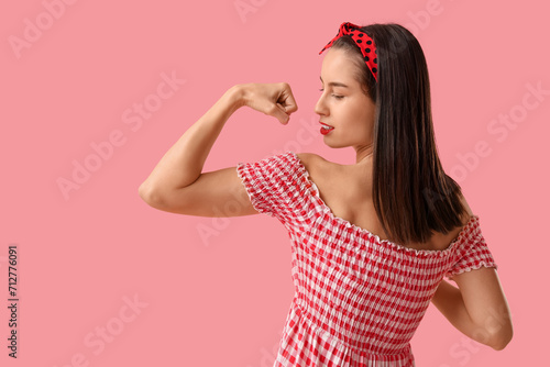 Portrait of strong pin-up woman showing muscles on pink background. Women's History Month photo