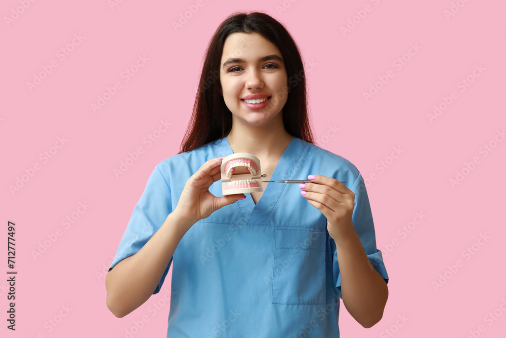 Female dentist with jaw model and tool on pink background. World Dentist Day