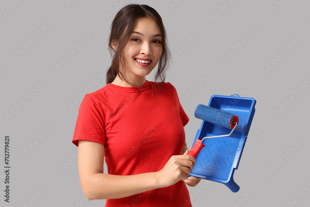 Young woman with paint roller and tray on grey background Young woman with paint roller and tray on grey background