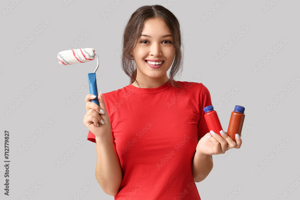 Young woman with bottles of paint and roller on grey background Young woman with bottles of paint and roller on grey background