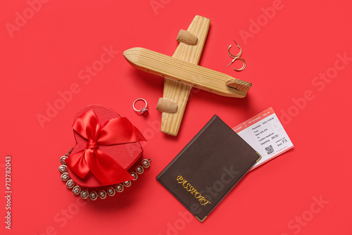 Passport with ticket, wooden airplane, gift and jewelry on red background. Valentine's Day celebration