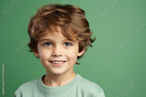 smiling little boy with curly hair looking at camera over green background