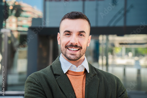 Front view of young adult man with friendly and positive expression. Close up portrait of handsome bearded guy with perfect white teeth smiling and looking at camera standing outdoors. Happy male photo