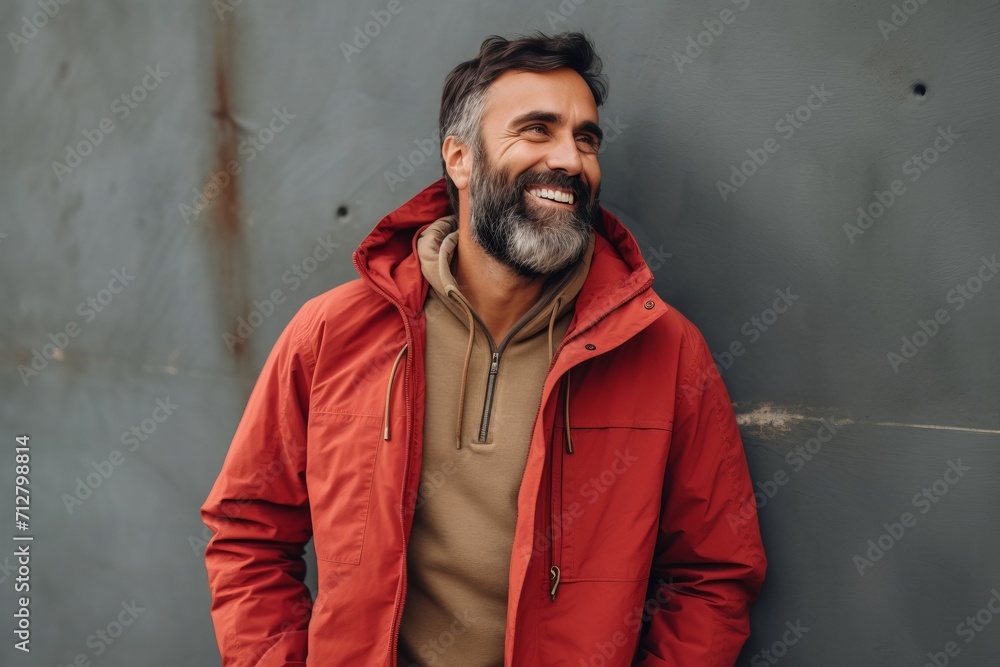 Handsome bearded man in a red jacket is looking at the camera and smiling.