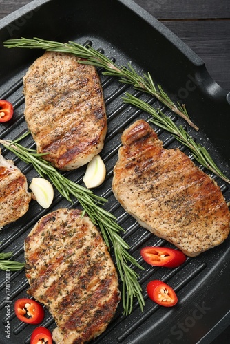 Grill pan with delicious pork steaks, garlic, chili pepper and rosemary on table, top view