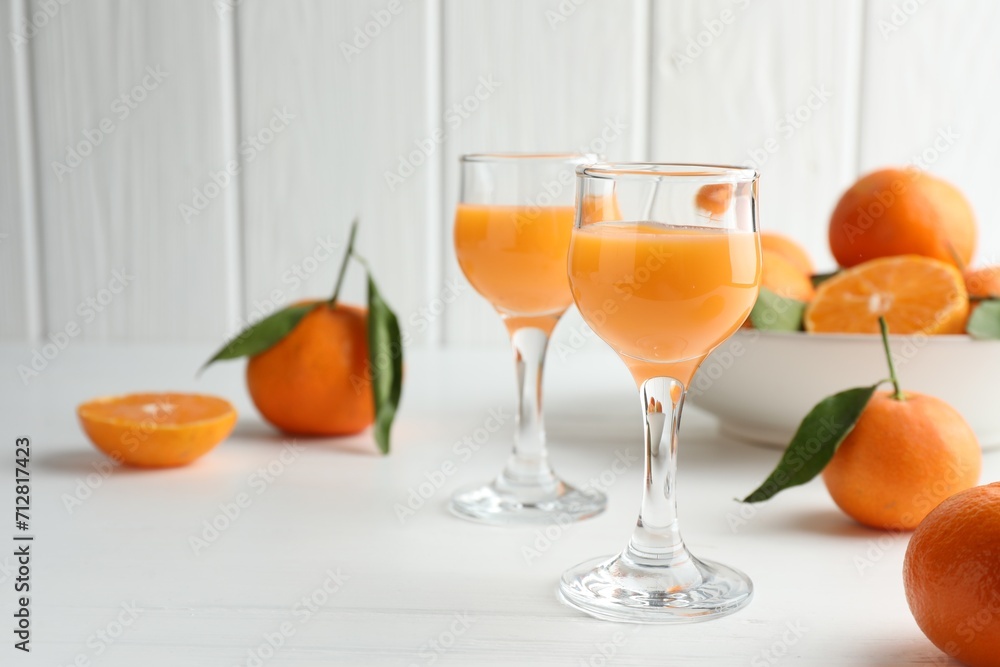 Tasty tangerine liqueur in glasses and fresh fruits on white table. Space for text
