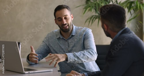 Sales manager consulting client in office, sit at desk make speech, explain contract details, selling company services. Two male colleagues brainstorming, discussing ideas and thoughts at workplace