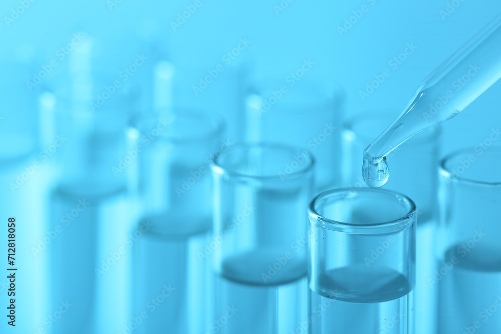Laboratory analysis. Dripping liquid from pipette into glass test tube on light blue background, closeup Laboratory analysis. Dripping liquid from pipette into glass test tube on light blue background, closeup