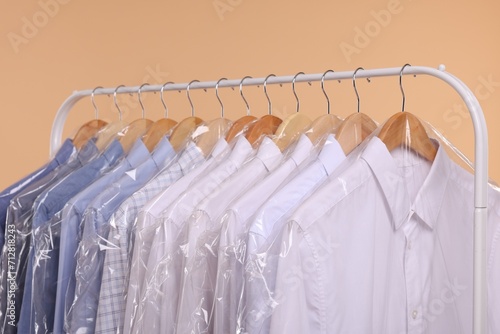Dry-cleaning service. Many different clothes in plastic bags hanging on rack against beige background