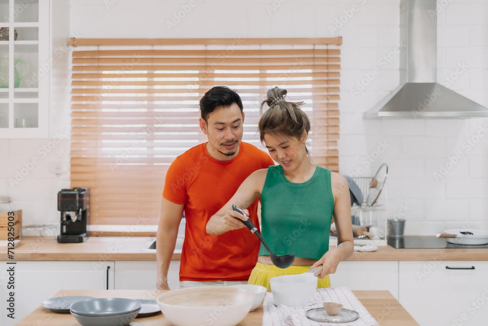 Husband looking at wife who cooking lunch for him. Happy asian couple in kitchen Husband looking at wife who cooking lunch for him. Happy asian couple in kitchen