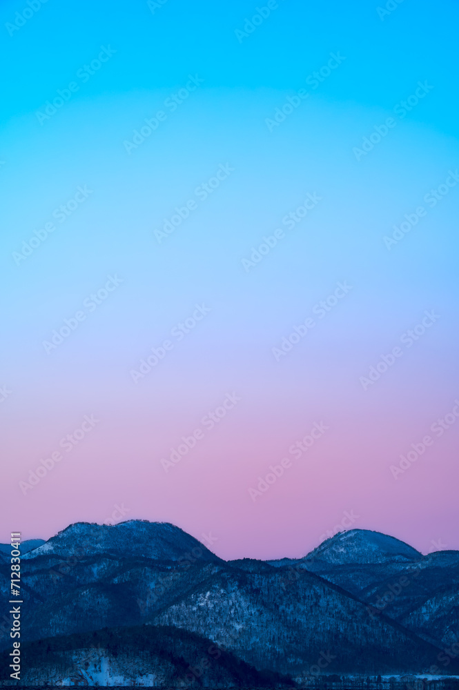 パステルカラーの夜明けの空と山々。