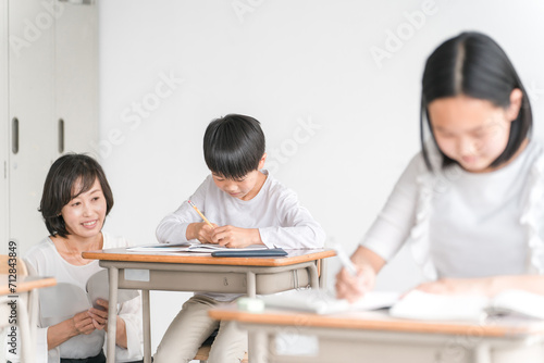 学校の教室・塾で先生と話す高学年のアジア人男子生徒（学童・児童クラブ・学童保育・学習・教育）  © buritora