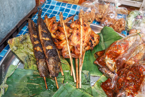 Various side dishes street food of thailand. Grilled catfish on skewers, grilled chicken on skewers and other side dishes in a tray with banana leaves on the stall.