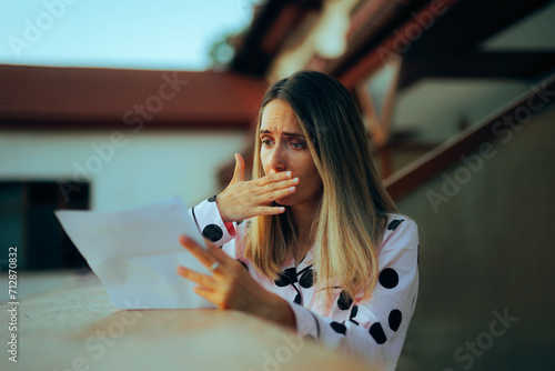 Surprised Woman Reading a Letter Document on the Balcony. Lady receiving an expensive overcharged invoice in the mail
 photo
