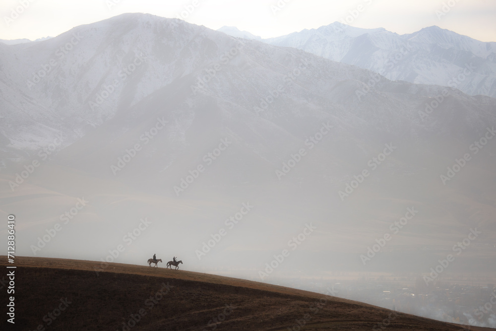 Two riders in view of Tian Sian mountains. Two little horsemen against large-scale landscape.