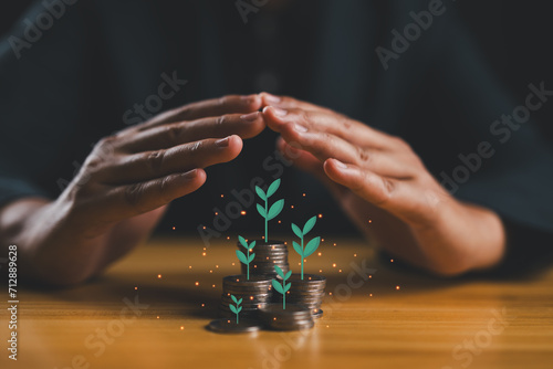 Hand protecting coins stacking with plant growth on the table. Money saving dividend yield and return profit investment concept. photo