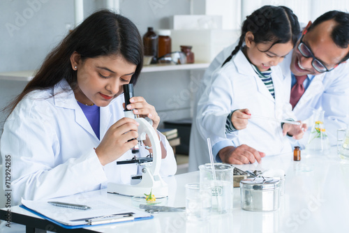 Indian scientist woman student using microscope do an experiment at biology class in school laboratory while teacher teaching another kid student. Education, science and school concept