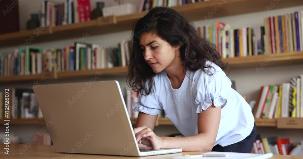 Pensive Indian business woman work on laptop in modern office, stand at desk, look at screen, search important information, make decision feel lack of ideas, read email, correspond to client distantly Pensive Indian business woman work on laptop in modern office, stand at desk, look at screen, search important information, make decision feel lack of ideas, read email, correspond to client distantly