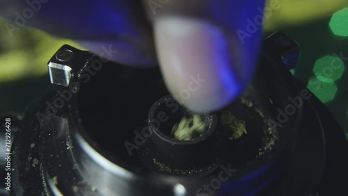 close up of a black mans hand as he slowly breaks up marijuana bud into the bowl of a vaporizer preparing to smoke the pot