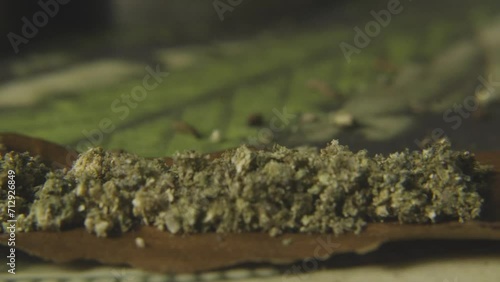 a black mans hand breaking up marijuana budss onto a hemp wrapper to prepare to roll a blunt photo