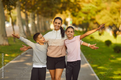 Portrait of happy smiling sporty family of mother and her children boy and girl wearing sportswear looking cheerful at camera after workout in park. Outdoors training and healthy lifestyle concept.
