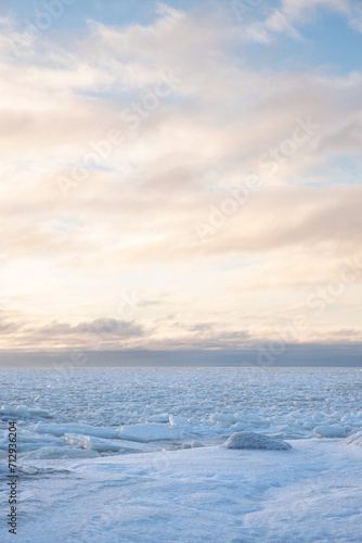 a snowy rock on the seashore under a colorful half-cloudy sky © Jarkko