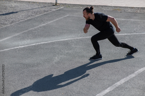Bearded man with long hair doing lunges on the sports field. 