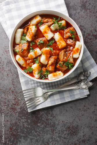 Boiled potato dumplings Kopytka with meat gravy close-up in a plate on the table. Vertical top view from above photo