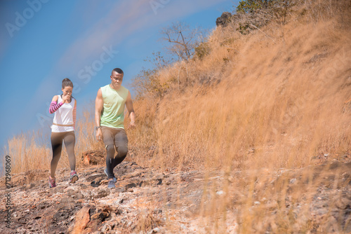 Young Ethnicity African American couple running trail outdoor activities at mountain in Autumn season, happy woman and man wearing sport wear spend time together jogging or training in sunny day © Rakchanok
