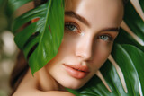 blue-eyed woman with freckles in the jungle peeks out from behind a tropical palm tree. Beautiful woman with green leave near face and body. Closeup girl's face with green leave