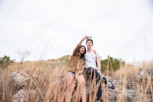 Young Asian tourists couple of hikers taking a selfie smiling with love, care and happiness together in summer. Partner or couple adventure travel together in forest summer stand on peak mountain.