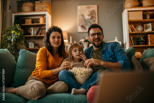 A family of three having a delightful time watching a film and snacking on popcorn