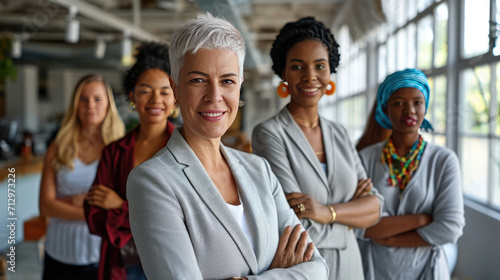 Group of diverse professional women confidently standing in a line, with the woman in the foreground crossing her arms, showcasing a strong and united front in a workplace setting.