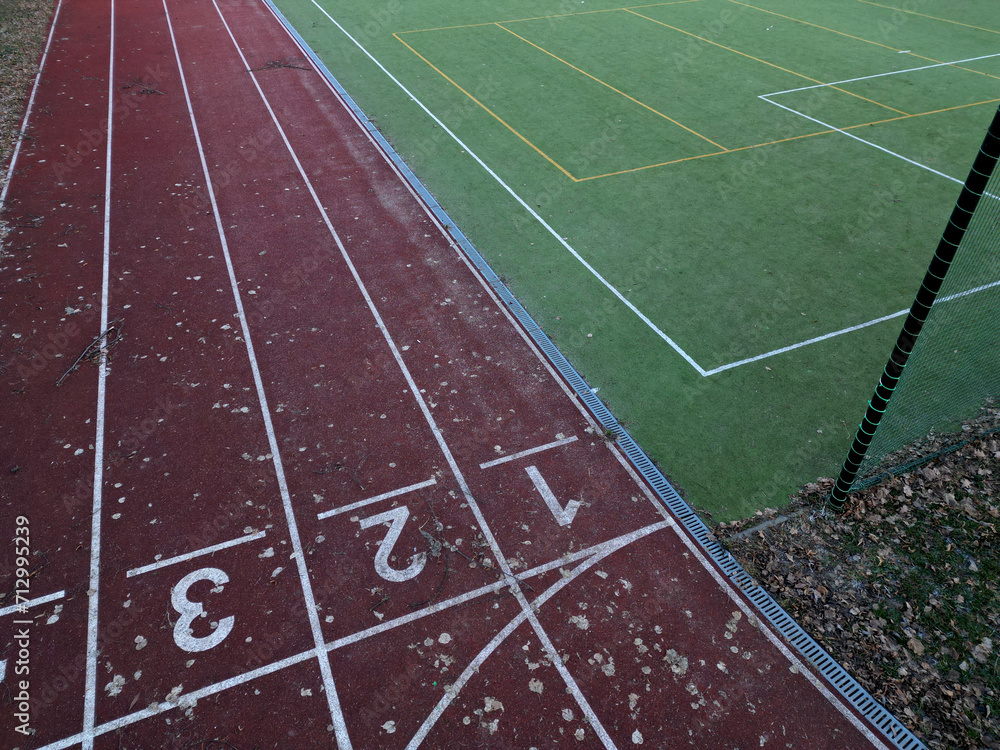 sports stadium with a running track with several lanes. inside oval there is a small football field for netball and handball with shield barriers. synthetic turf. view from top, all weather track