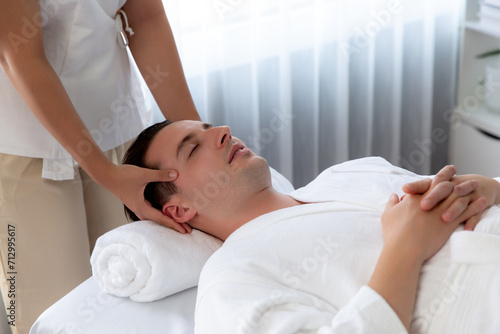 Caucasian man enjoying relaxing anti-stress head massage and pampering facial beauty skin recreation leisure in dayspa modern light ambient at luxury resort or hotel spa salon. Quiescent